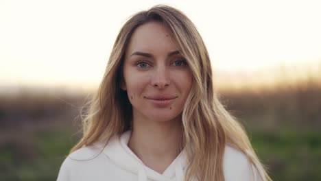 natural blonde woman look at camera outdoors with blurred background