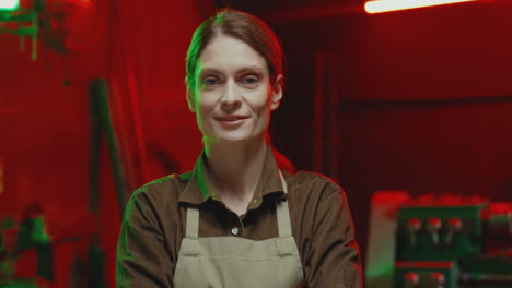 caucasian young woman welder wearing apron and looking at camera with arms crossed in workshop