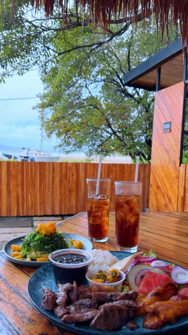 Traditional Costa Rican meal served at outdoor tropical restaurant. Grilled meat with rice, beans, salad and iced drinks on wooden table.