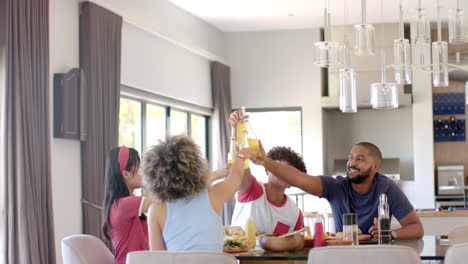 diverse friends toasting with drinks, enjoying meal together at home dining table