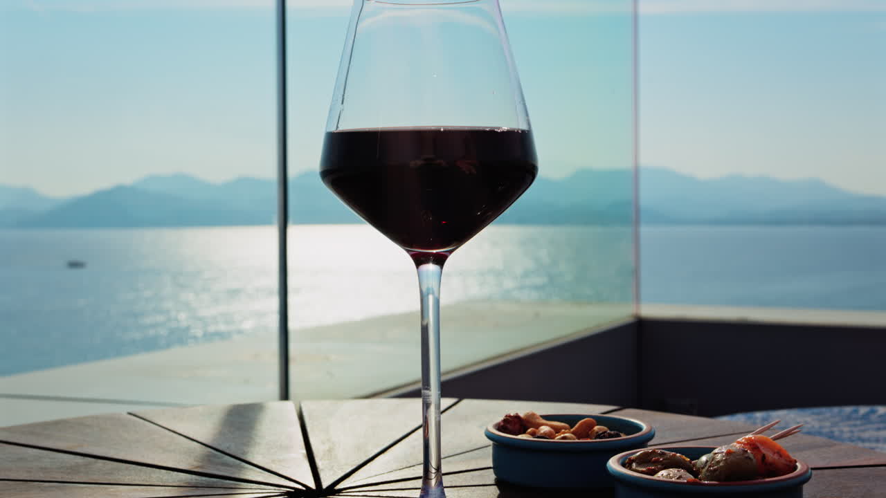Close up of a glass of red wine and snacks on a table at a terrace with a sea view