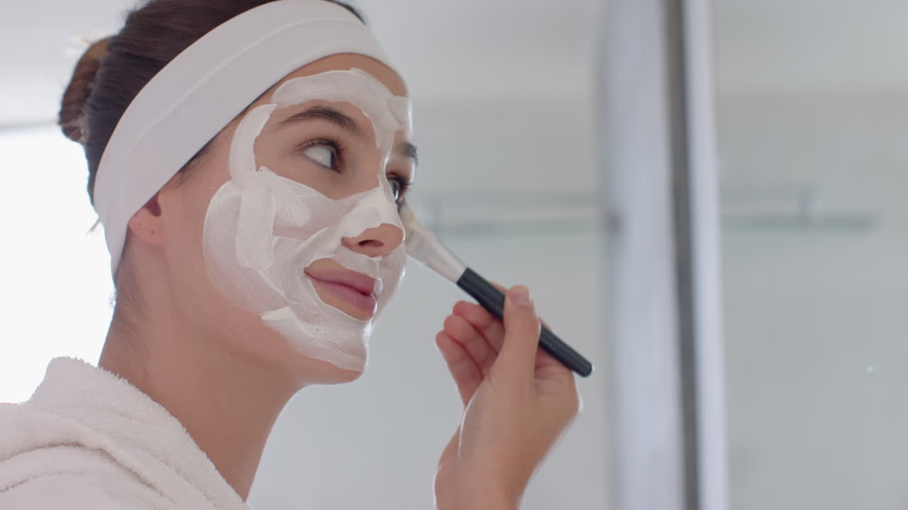 Applying face mask, woman smiling and using brush for skincare at home spa