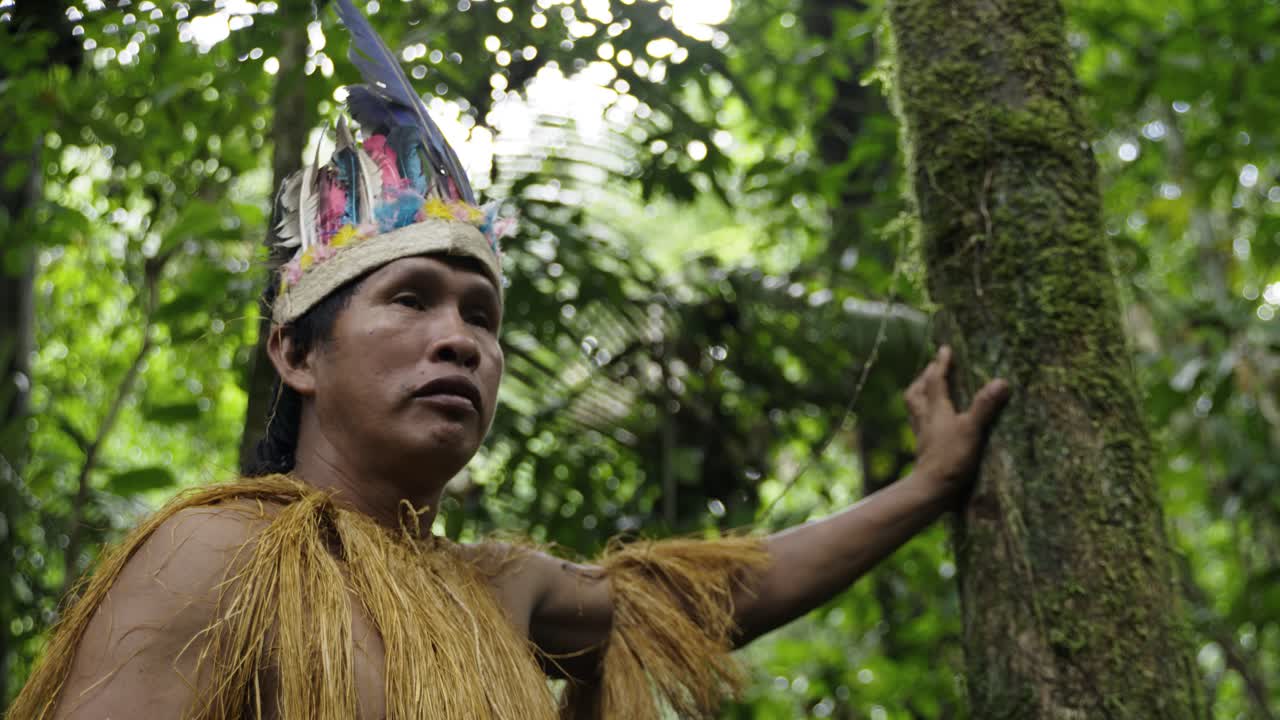 retrato de un hombre indígena con un sombrero de plumas y una camisa con flecos en el denso bosque del amazonas, letizia, colombia