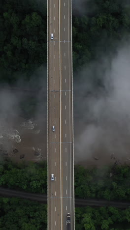 vertical drone shot of bridge traffic above deep new river gorge and clouds, west virginia usa