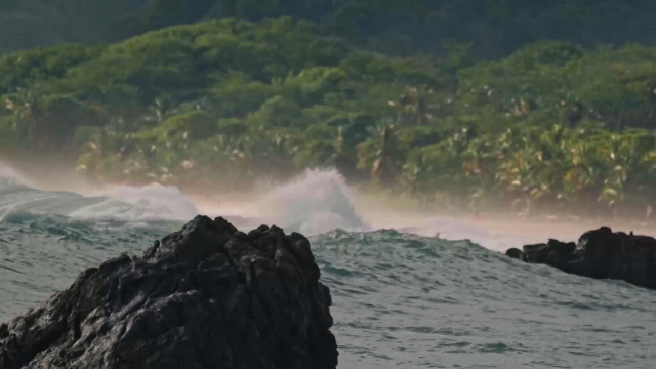 A powerful wave crashes against the rocky shoreline of Santa Teresa, sending a dramatic spray of white water into the air