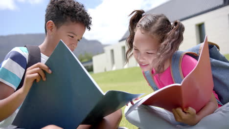 biracial boy and girl are engrossed in reading colorful folders outdoors in school