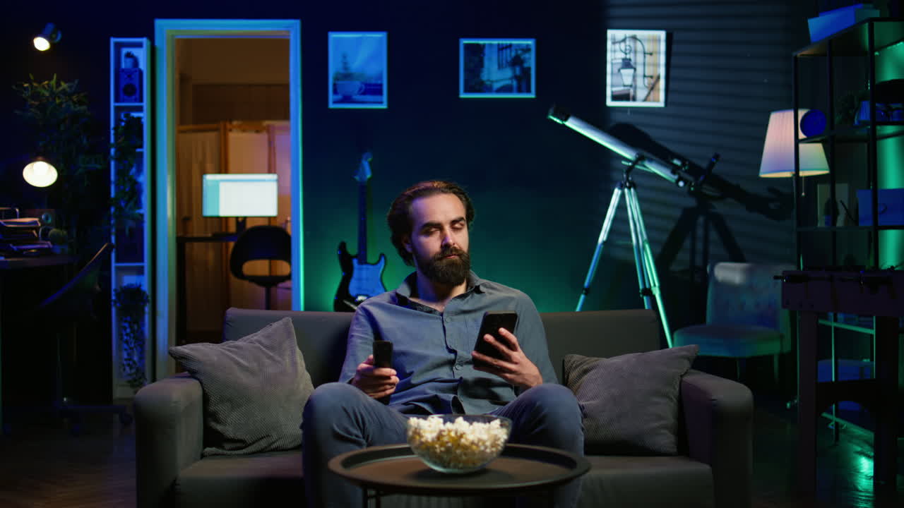 persona viendo la televisión, enviando mensajes de texto a un amigo en el teléfono móvil, sosteniendo el control remoto