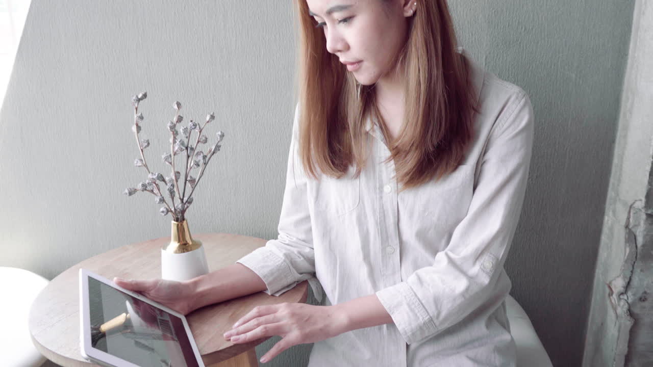 若いアジア人女性がタブレットを使い、カメラに向かって微笑んでいる。