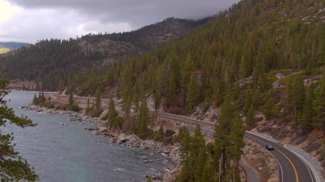 Aerial of road curving around Lake Tahoe in Nevada with cars driving past on a cloudy winter day
