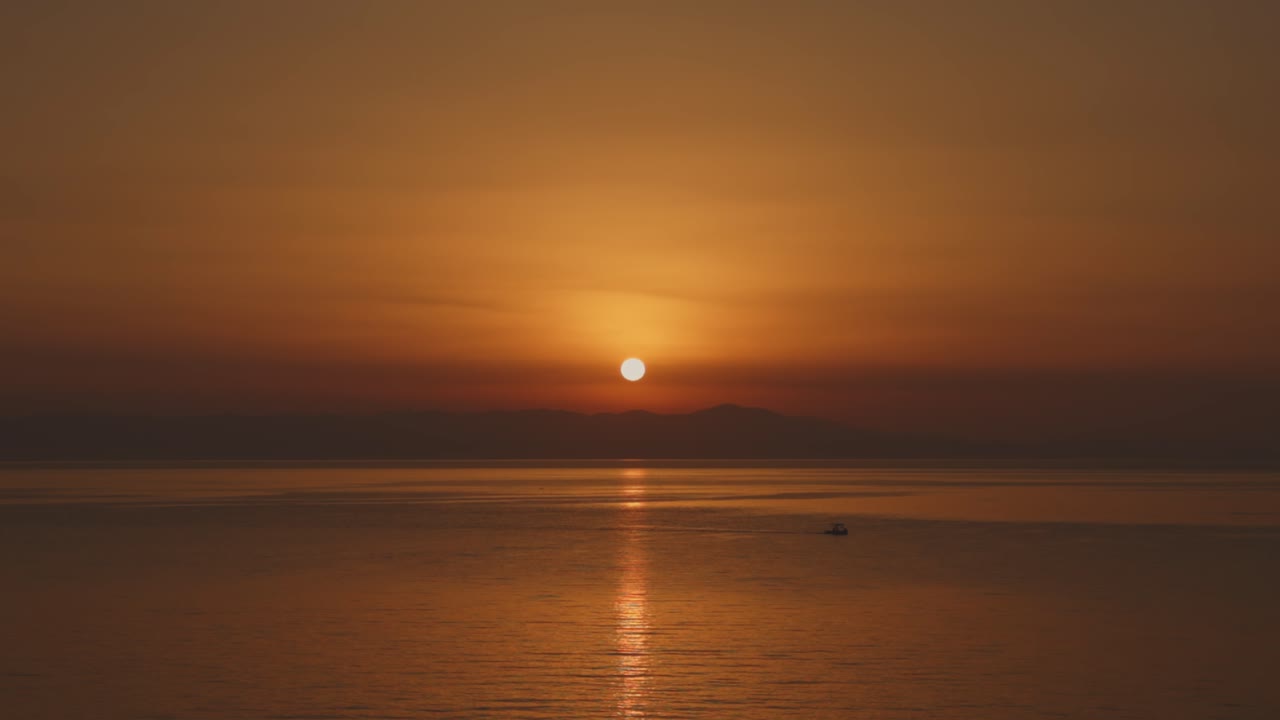 A beautiful sunset over the Aegean Sea, casting golden hues over the water and distant island.
