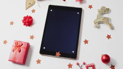 video of red christmas present, with decorations and tablet on white background