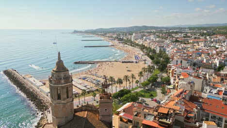 Drone-captures-aerial-footage-of-an-ancient-church-overseeing-coastal-town-by-sea-on-a-sunny-day