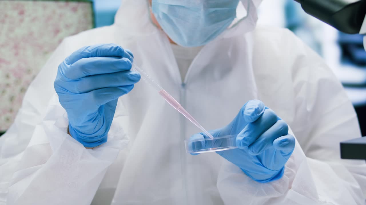 Scientist in Protective Suit Pipetting Liquid into Petri Dish in Laboratory