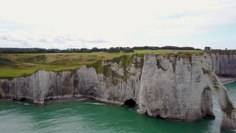 voando em direção à terra, ao lado do arco rochoso de etretat, na frança