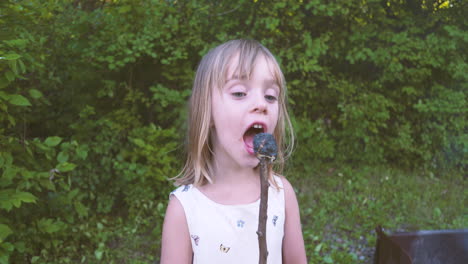 Little-girl-takes-a-bite-out-of-a-burnt-marshmallow-on-a-stick