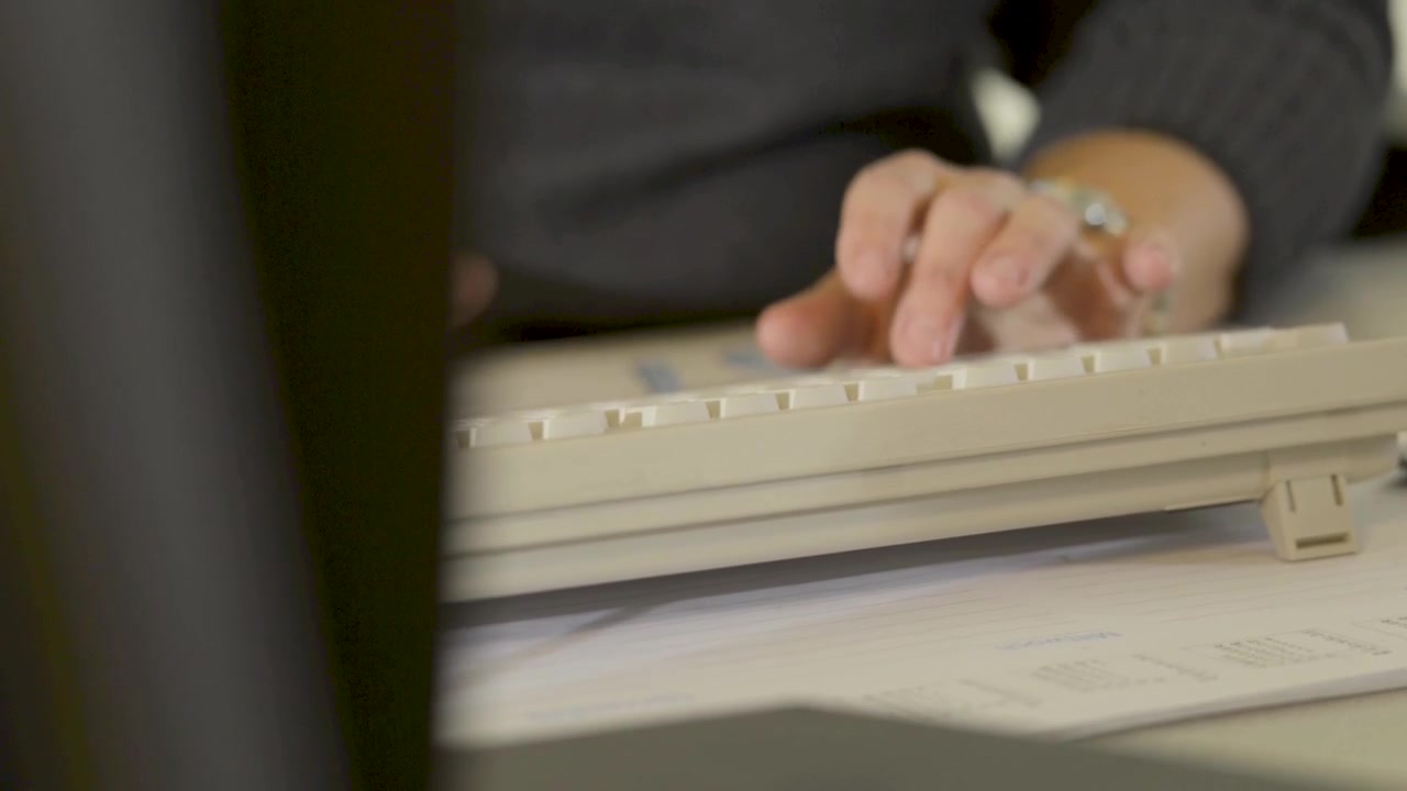 Mani che digitano sulla tastiera del computer alla scrivania con documenti, scena d'ufficio ravvicinata