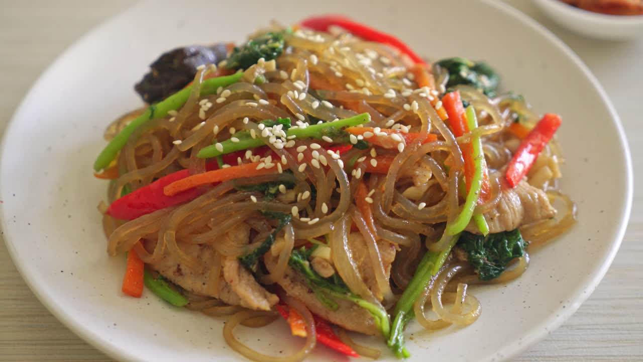 japchae o fideos vermicelli coreanos salteados con verduras y cerdo cubiertos con sésamo blanco - estilo de comida tradicional coreana