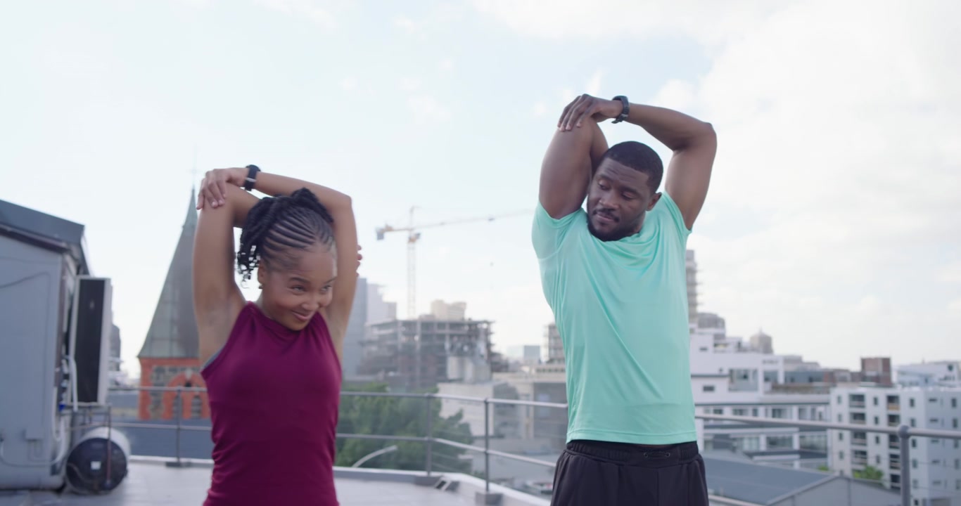 African friends in gymwear mirroring man's raise, stretching for warmup on roof railing with watch