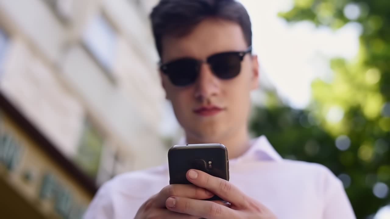 Caucasian man in white shirt and sunglasses writing messages on the phone. Close up from the bottom