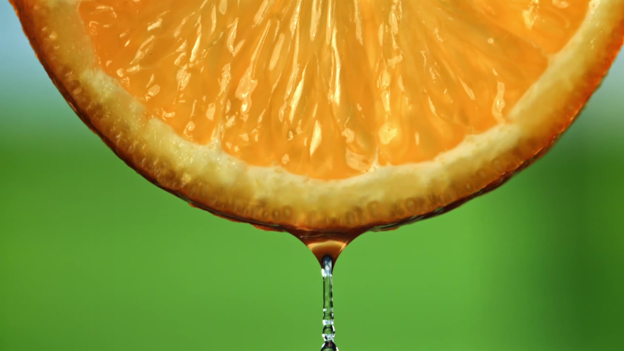 Primo piano di una fetta d'arancia fresca con acqua che gocciola al rallentatore
