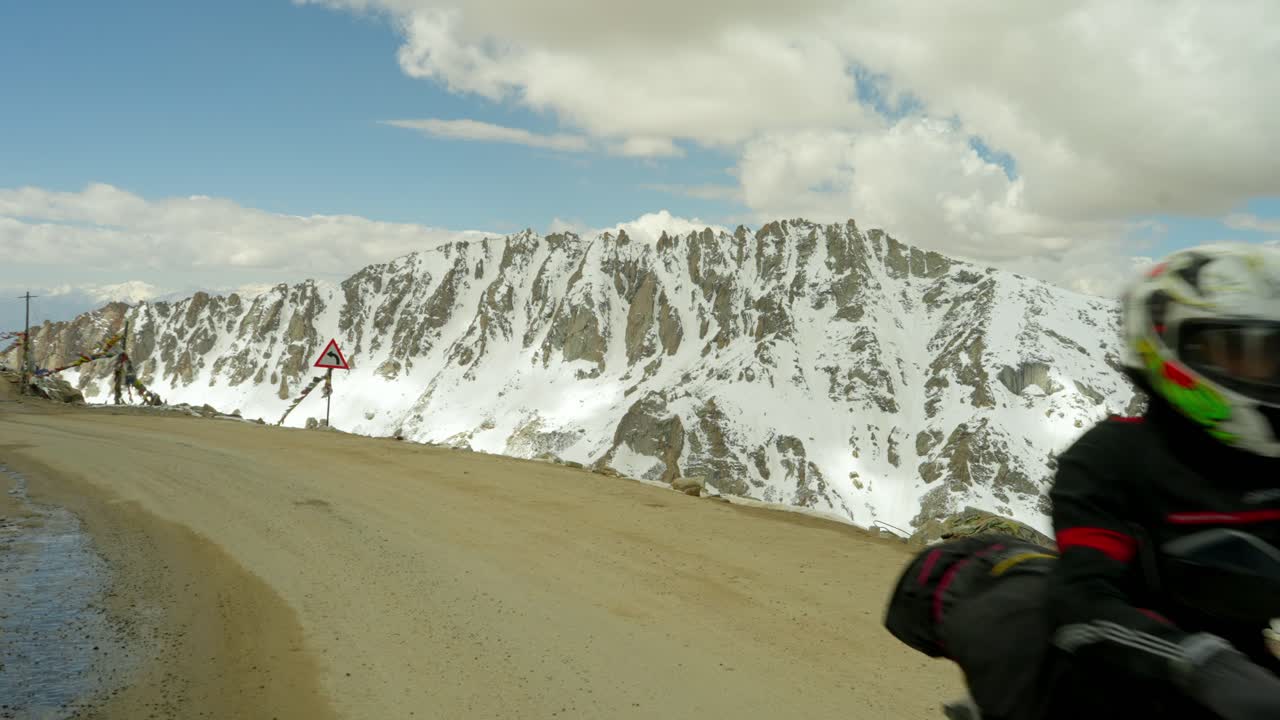 Biker riding on Himalayan road in Ladakh, India with snow on mountains in backdrop, stunning high-altitude landscapes in the snow