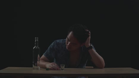 drunk, depressed asian man drinking vodka from the bottle in black background