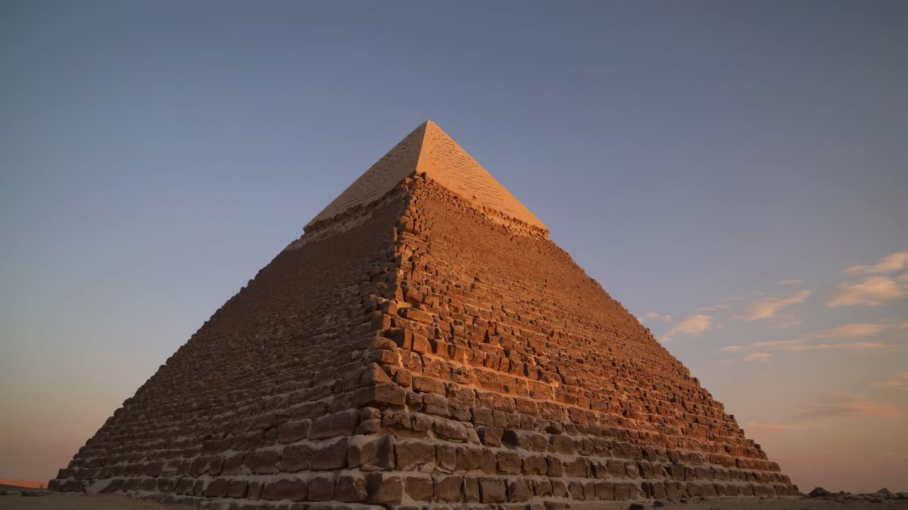 Low-angle shot of a pyramid under a clear sky at sunset, capturing its grandeur and historical