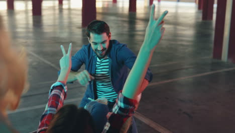 close-up view of cheerful caucasian man having fun with two girls while carrying them in the trolley in a empty parking