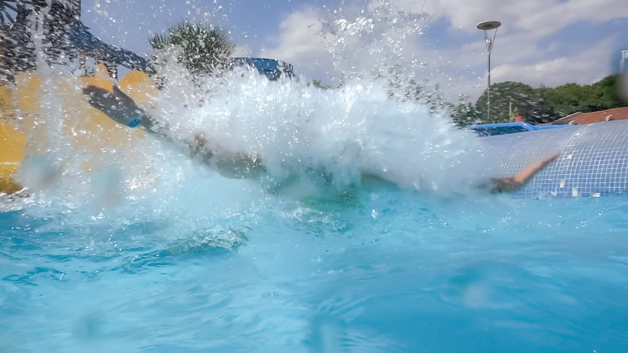 descenso del tobogán acuático en un parque acuático de vacaciones. cámara lenta en un tobogán acuático vacaciones familiares, una mujer en bikini desciende del tobogán en una piscina de agua azul salpicando gotas de agua.