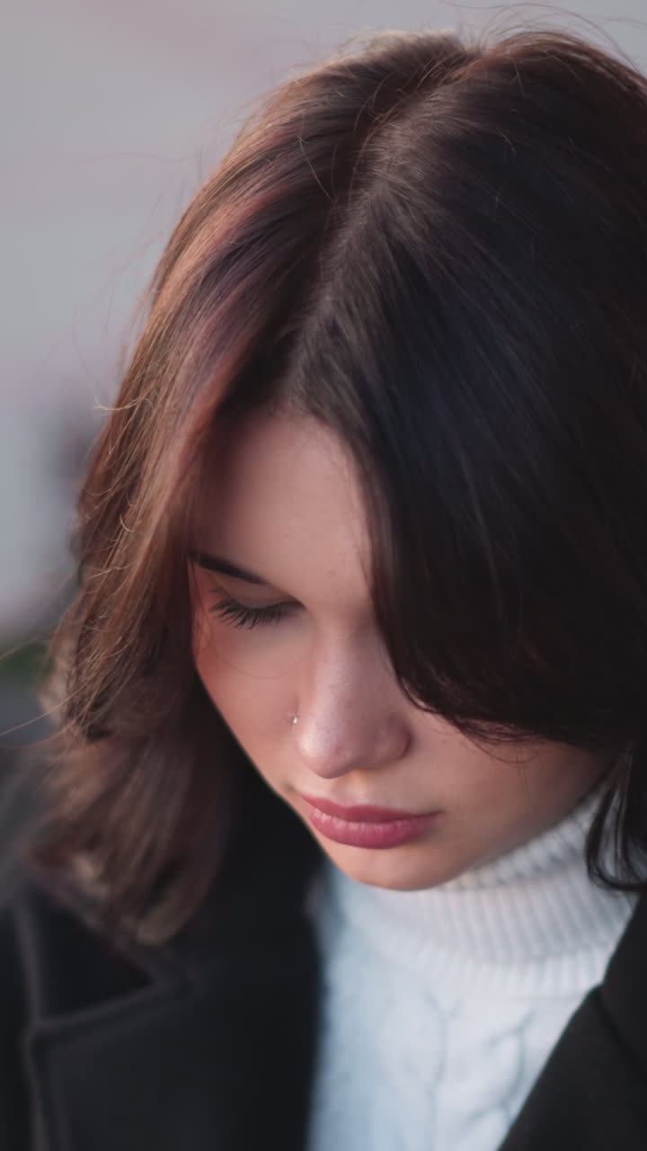 야외에서 앉아있는 사려 깊은 젊은 여성은 색 터틀과 검은색 코트를 입고, 부드러운 갈색 머리카락이 얼굴을 틀고, 평온하고 내면적인 분위기를 만니다.