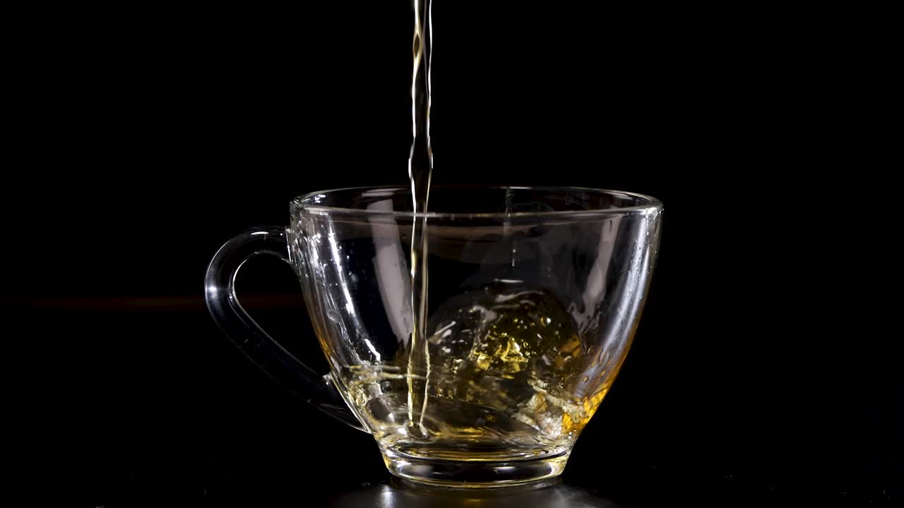 A sequence of tea being poured into a transparent glass cup against a dark backdrop, highlighting fluid motion and golden hues