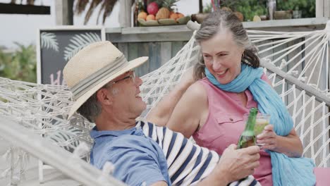 una pareja caucásica feliz bebiendo y hablando en una hamaca fuera del bar de la playa, en cámara lenta.