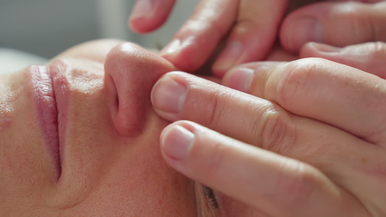 Skin care expert massages client brow area with gentle fingertip pressure, releasing tension as patient shifts from slight tension to relaxed state in serene spa setting under soft ambient lighting