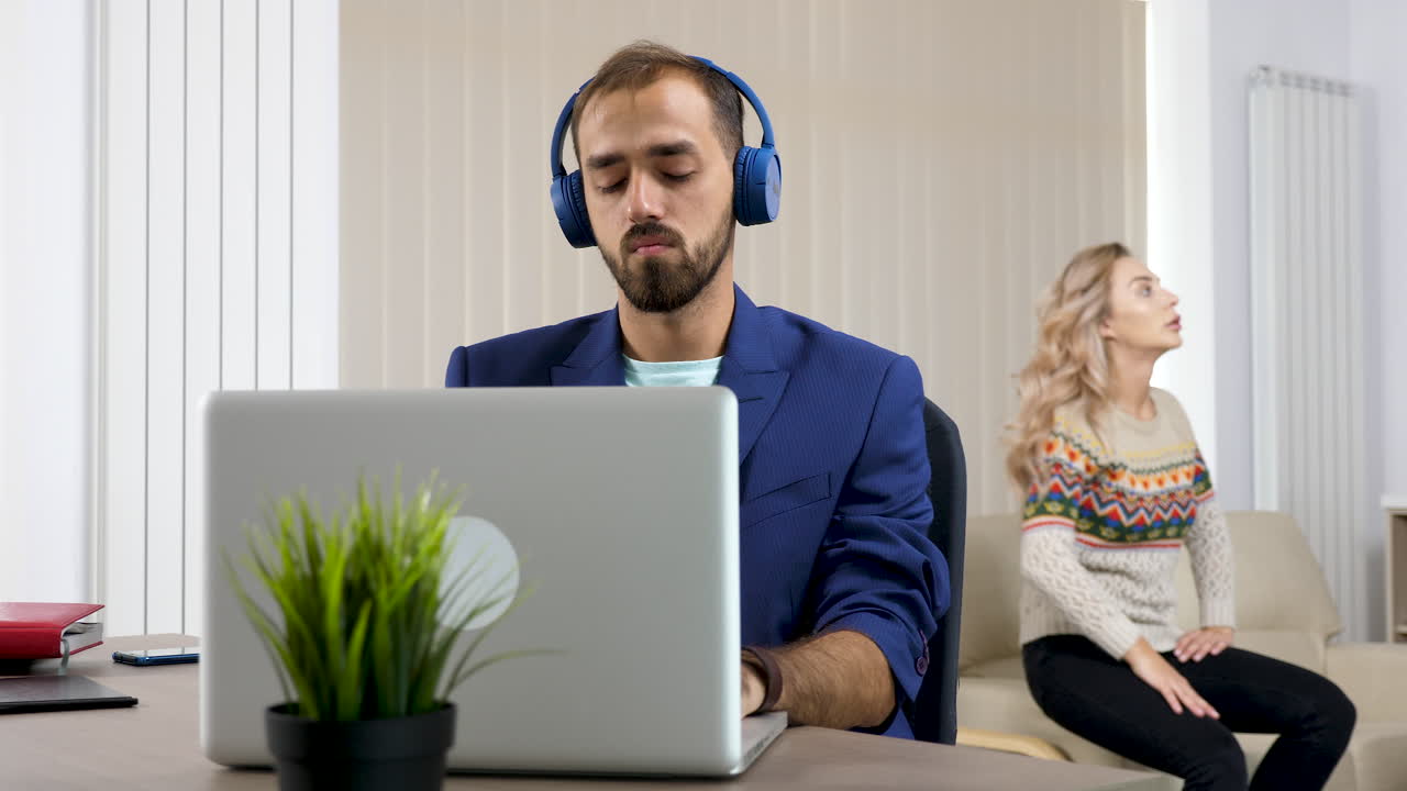 Man working on laptop while woman displays signs of discomfort