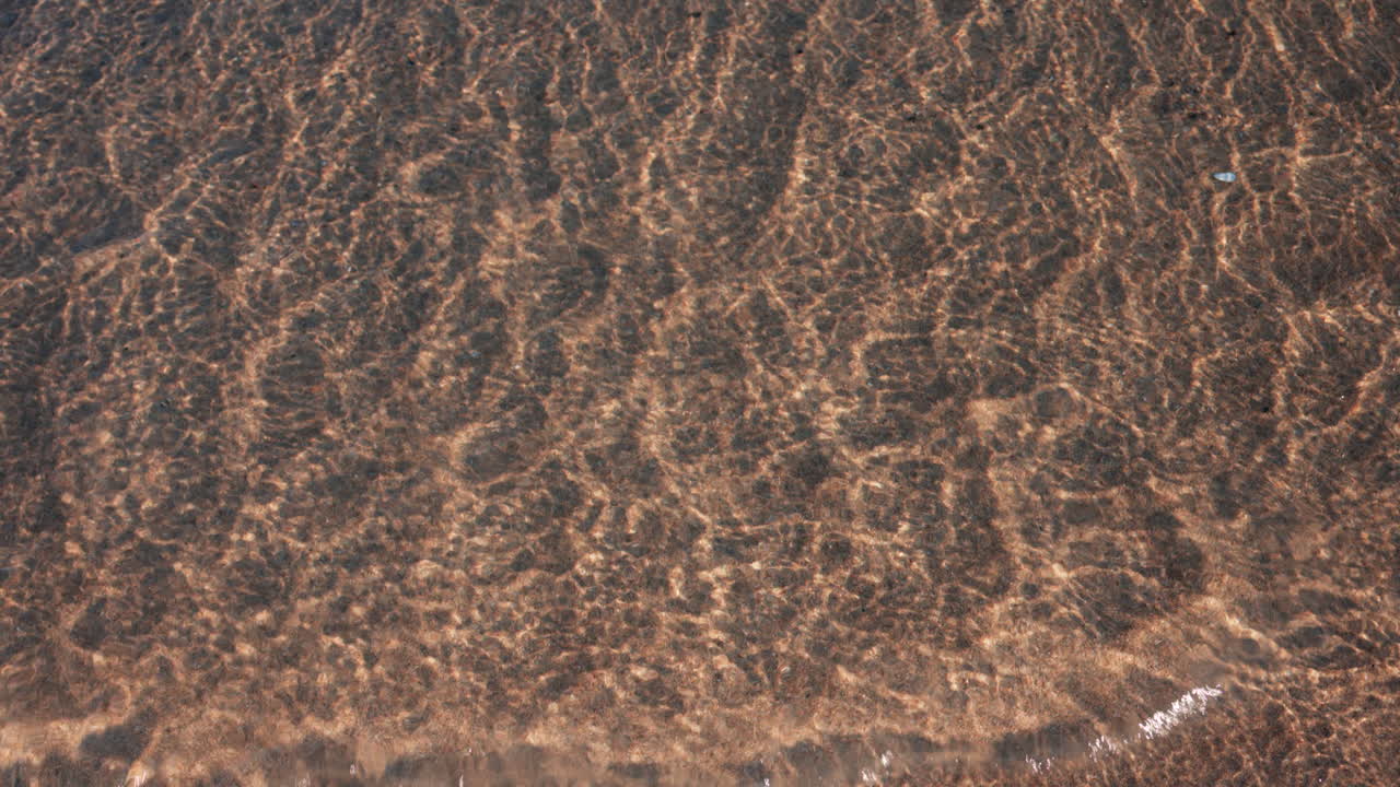 Close up of small waves rolling gently onto the sandy beach under morning light