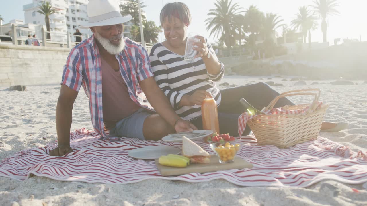 Coppia anziana afroamericana felice che fa un picnic in spiaggia, al rallentatore