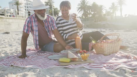 happy senior african american couple having picnic at beach, slow motion