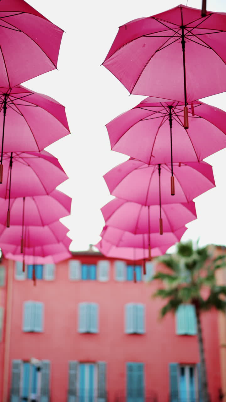 Rows of pink umbrellas above the streets of the old town in Grasse, France. Vertical