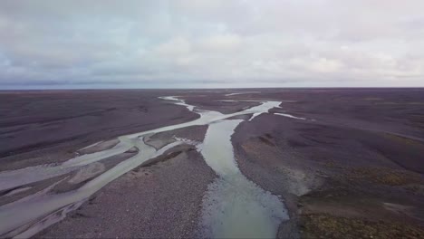 Flyover-and-ascend-over-braided-glacial-river-flowing-through-stark-Iceland-landscape