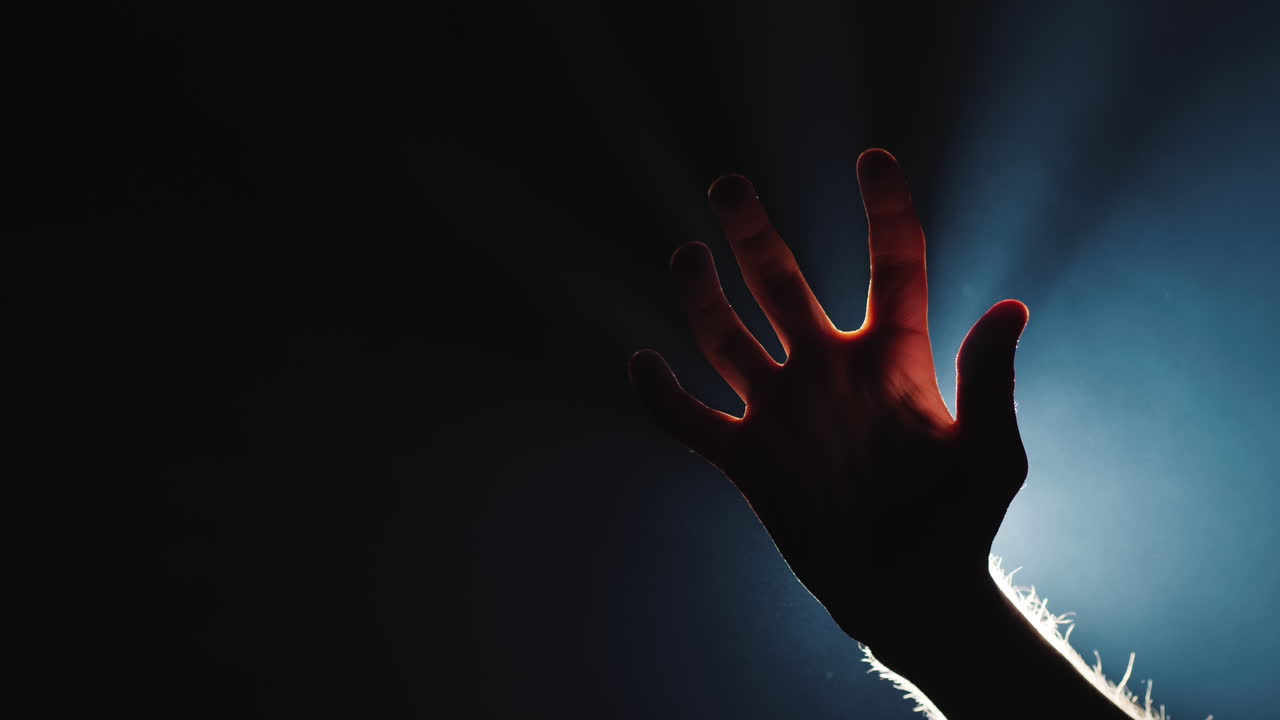 la silueta de la mano de un hombre en la oscuridad de los dedos vienen los rayos de luz