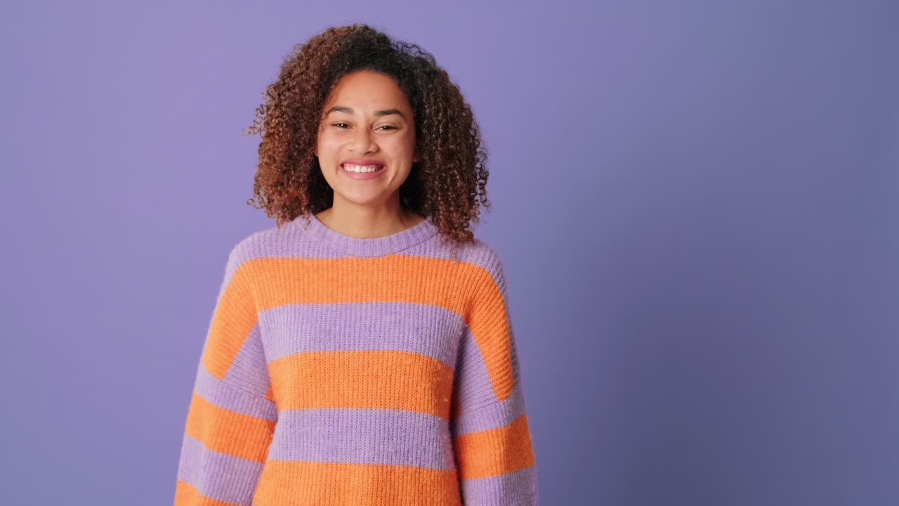Smiling Young Woman with Curly Hair Waving Hello on Purple Background