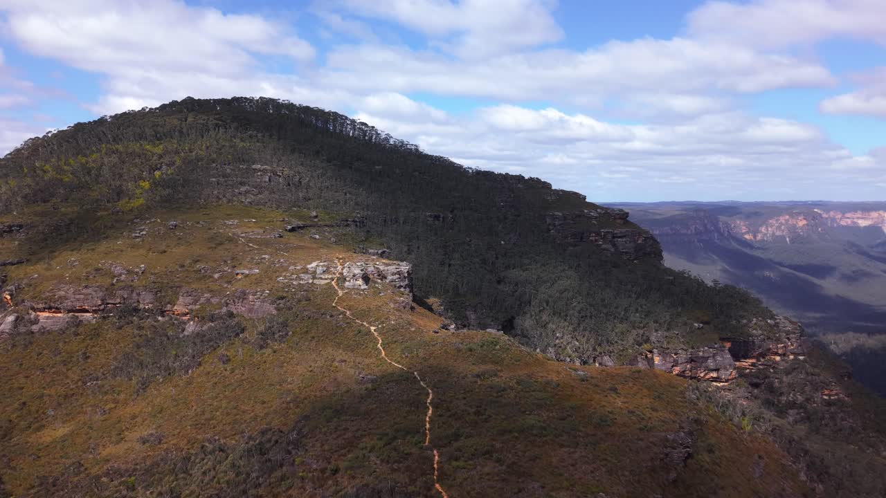 High altitude flyover of golden-lit mountain tops and lush valleys filled with dense gum forest, NSW Australia