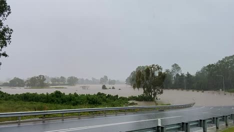 Queensland,-New-South-Wales,-Australien,-Überschwemmungen-Im-Februar---Eine-Verlassene-Straße-In-Einem-Vorort-Von-Brisbane-Krümmt-Sich-Nach-Unten-Und-Verschwindet-In-Flutwasser,-Während-Sintflutartiger-Regen-Vom-Grauen-Himmel-Fällt