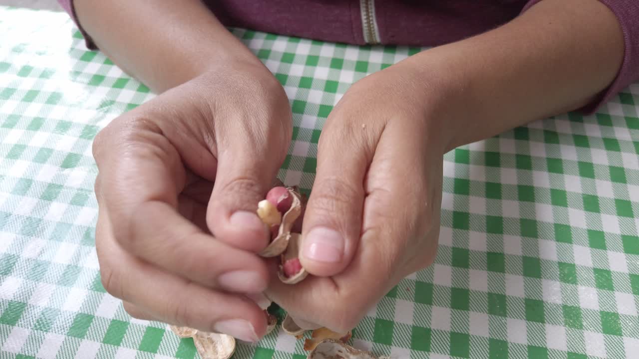 Close-up shot of person cracking peanut shells and peeling nuts on green checkered tablecloth