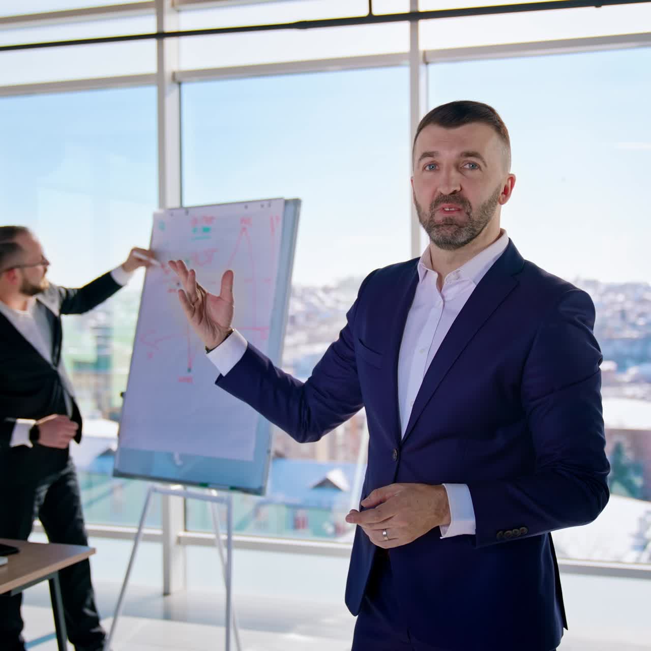 Portrait of executive man in office center. Business people working at new blueprint on the window city background. Handsome businessman in suit talking on camera