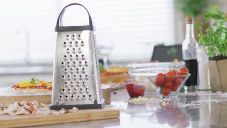 Cheese-grater,-tomatoes-and-sliced-mushrooms,-pizza-ingredients-on-kitchen-counter