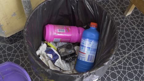 una cámara gopro dañada es desechada en una bolsa de basura de plástico negro, colocada en un cubo de basura