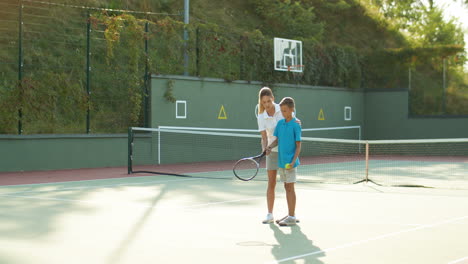 mujer enseñando a su hijo adolescente a jugar tenis en un día de verano 2