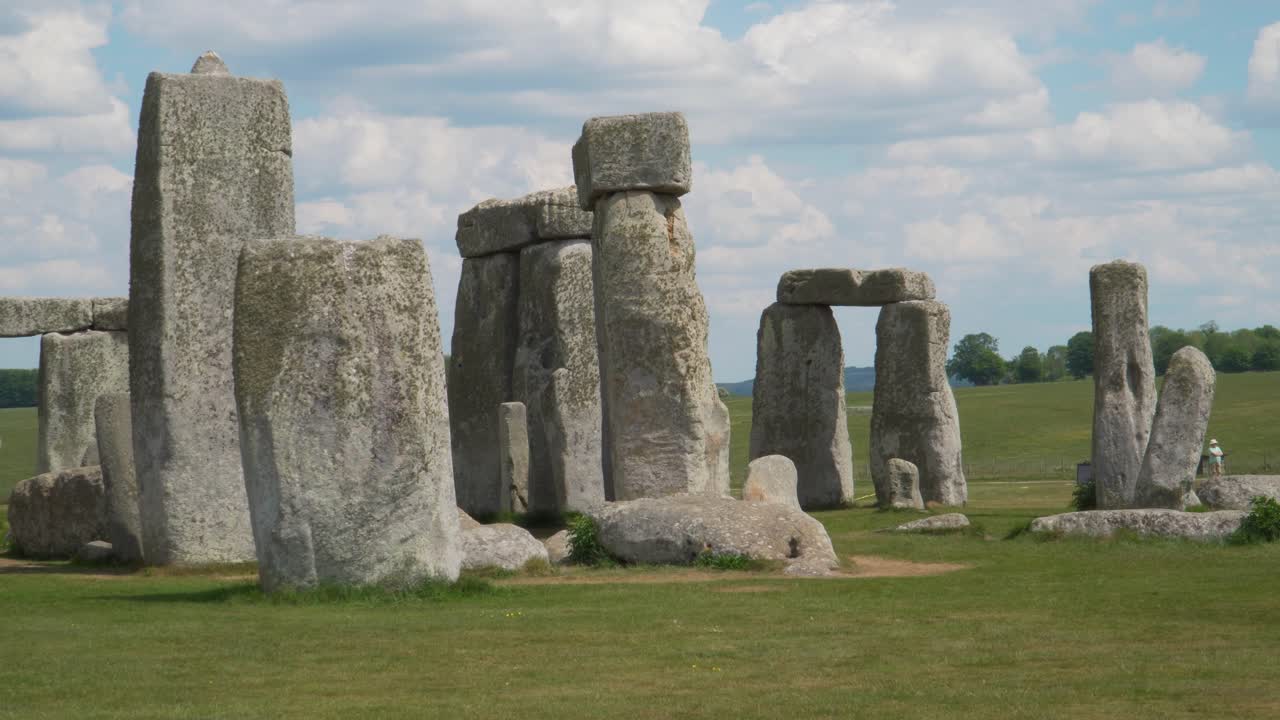 Close up view to the Stonehenge a prehistoric megalithic structure on Salisbury plain in Wiltshire England. Steady camera with a group of tourists and cloudy sky in the background. Grass movement.