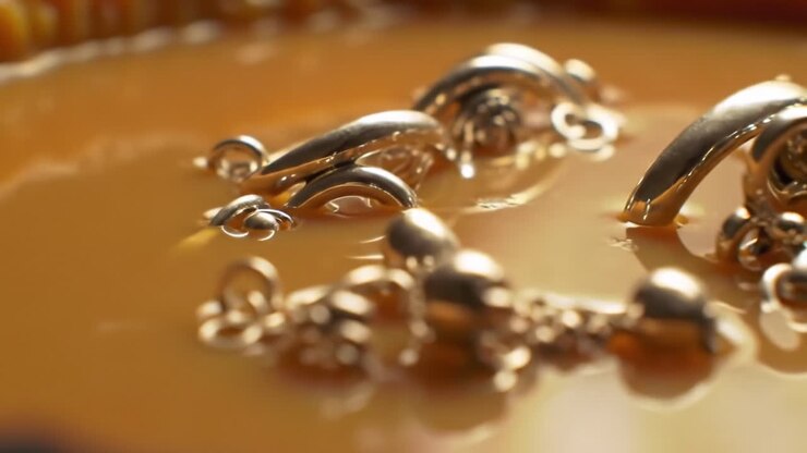 Elegante gioiello d'oro immerso in un ricco liquido ambrato durante un progetto di arte creativa in uno studio soleggiato
